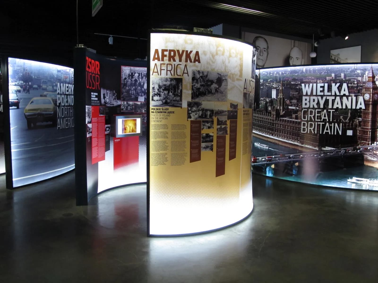 A museum exhibit features illuminated curved panels with text and images about different regions like Africa, North America, USSR, and Great Britain.